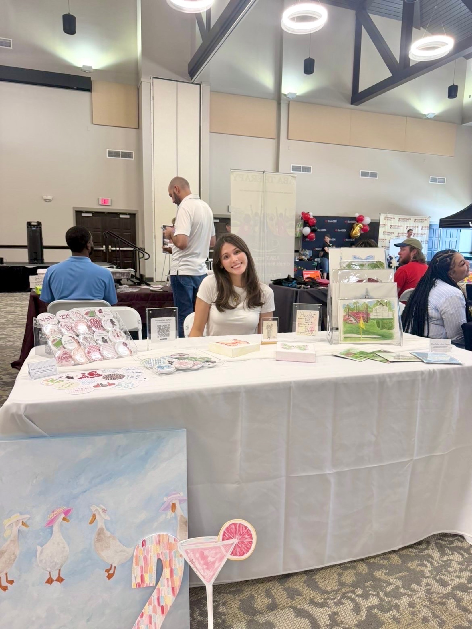 Chamberlain Marie at her art table with paintings, paper goods, and collegiate pieces